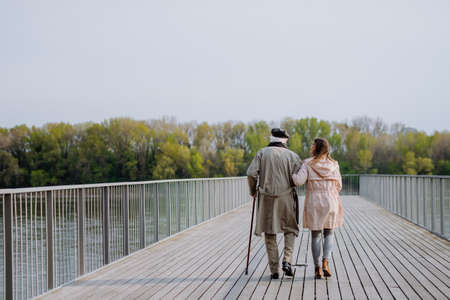 Rear view of senior man with daughter outdoors on a walk on pier by river.の写真素材
