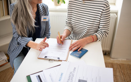 Senior woman volunteer helping Ukrainian woman to fill in forms at asylum centre.の写真素材