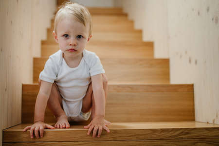 Cute little boy sitting on stairs at home and looking at camera.