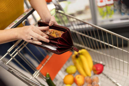 Worried woman checking her wallet when shopping in supermarket. Inflation and economic recession...