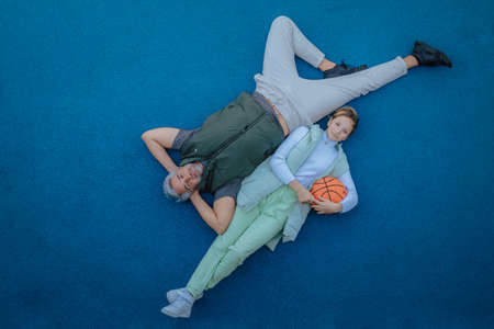 Top view of happy father and teen daughter lying and looking at camera outside at basketball court.