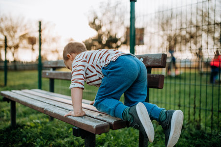Little boy climbing up the bench on outdoor playground.