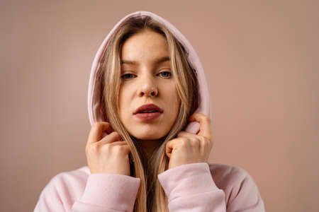 Fashion studio portrait of a happy young blonde woman in hoodie posing over pink background.の写真素材