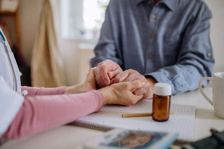 Close-up of doctor holding hands of senior patient and consoling him during medical visit at home.の写真素材