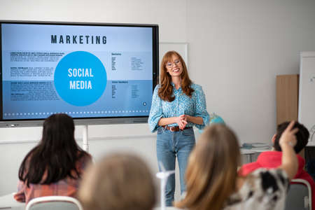 Young High school teacher giving marketing lesson to students in classroom
