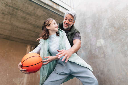 Happy father and teenage daughter playing basketball outside at court.の写真素材