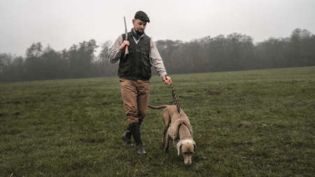 Hunter man with dog in traditional shooting clothes on field holding shotgun.の写真素材