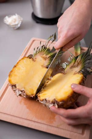Unrecognizable man cutting a pineapple on chopping board.