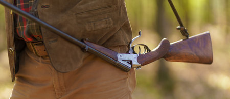 Close-up of hunter man carrying his rifle gun in forest.