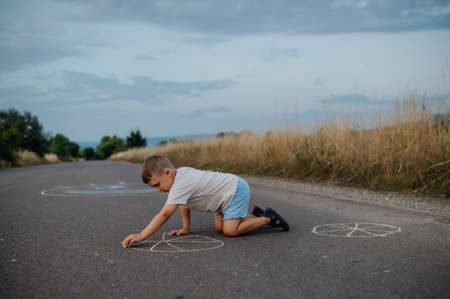 Little kid boy drawing with chalk on asphalt in summer.の写真素材