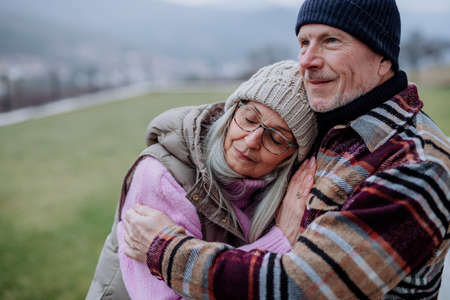 Senior man hugging and consoling his upset wife outdoors in garden in winter.の写真素材