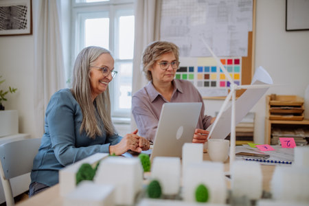 Senior women eco architects with blueprints working on laptop together in office.の写真素材