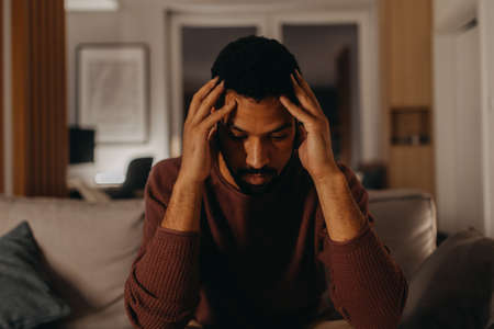 Portrait od depressed young African - American man with head in hands sitting at home.