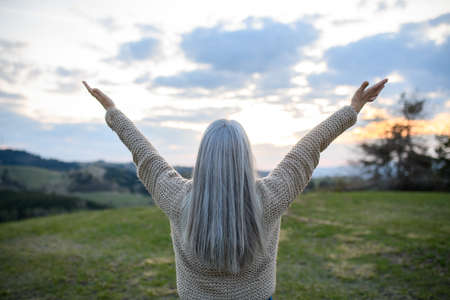 Rear view of senior woman with arms outstretched and face up at park on spring dayの写真素材