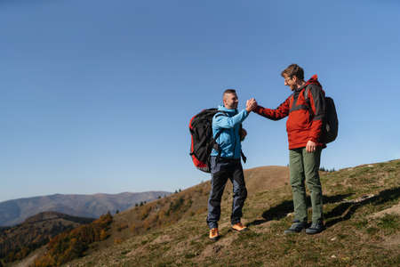 Paragliders high fiving after walking up hill to paragliding starting point, on a sunny morning in...