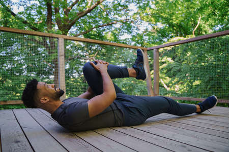 Happy young man stretching outdoors on terrace of tree house, weekend away and digital detox...