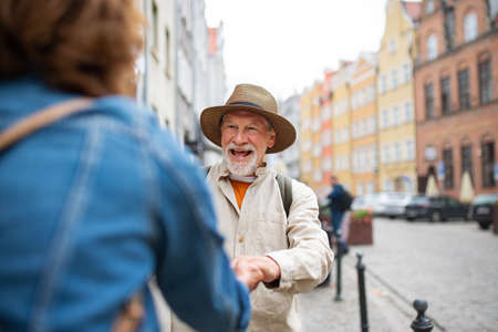 Happy senior man giving hand to senior woman, couple in love holding outdoors in townの写真素材