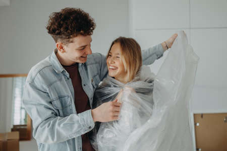 Cheerful young couple in love in their new apartment, having fun with wrapping foil. Conception of moving.の写真素材