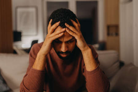 Portrait od depressed young African - American man with head in hands sitting at home.