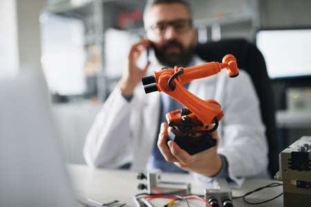 Robot arm industrial miniature figure in hand of robotics engineer working on laptop in laboratory.の写真素材