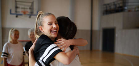 Group of young and old women, sports team players, in gym celebrating victory, hugging.