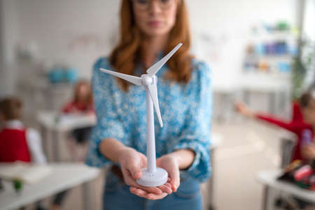 Close up for elementary school teacher holding model of wind turbine and learning kids about eco-friendly forms of renewable energyの写真素材