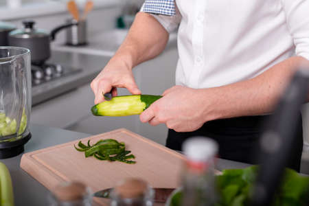 Man preparing vegetarian food meal peeling cucumber on cutting board. Homemade mealの写真素材