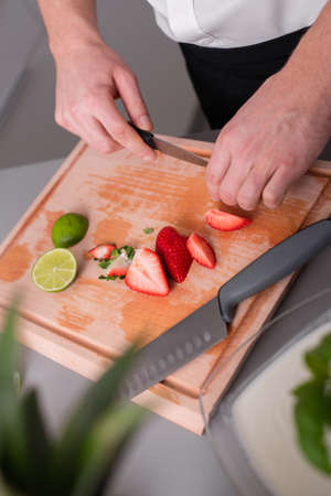 Man cutting strawberries and limes on chopping board.