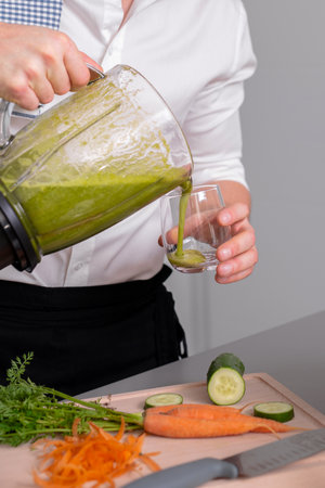 Unrecognizable man making green homemade smoothie in blender and pouring to glass. Healthy lifestyle concept.の写真素材