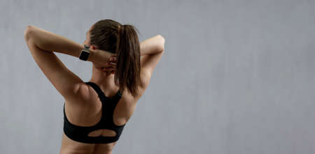 Rear view of young sporty woman in sports clothes stretching arms against grey background, copy spaceの写真素材