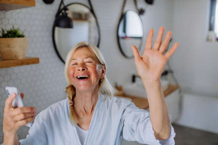 Cheerful senior woman in bathrobe listening to music in bathroom, relax and wellness concept.の写真素材