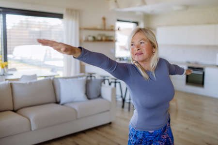 Fit senior woman doing stretching exercise at home, active lifestyle concept.