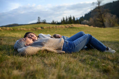 Happy senior grandmother with teenage granddaguhter lyinf down on grass in nature on spring day.