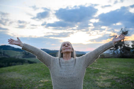 Senior woman with arms outstretched and face up at park on spring dayの写真素材