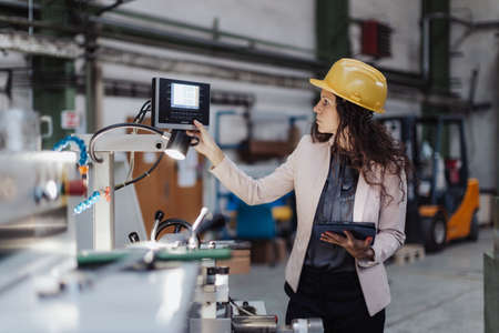 Portrait of female chief engineer in modern industrial factory using tablet and machine.