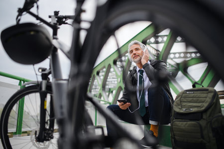 Businessman with bike sitting on bench, using smartphone. Commuting and alternative transport...