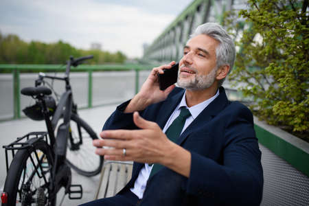Businessman with bike sitting on bench, using smartphone. Commuting and alternative transport conceptの写真素材