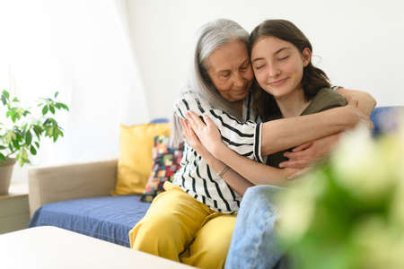 Senior grandmother with teenage granddaguhter having good time together at home, hugging.の写真素材