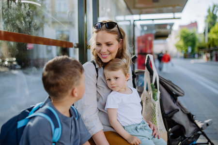 Young mother with little kids waiting on bus stop in city.の写真素材