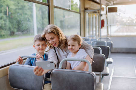 Young mother with little kids travelling in tram in summer and taking selfie.の写真素材