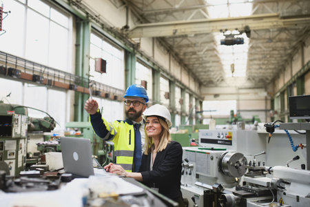 Male and female industrial engineers discussing factorys new machinery project and using laptop.