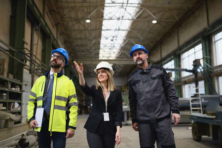 Manager supervisors and industrial worker in uniform walking in large metal factory hall and...