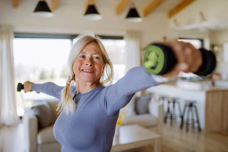 Fit senior woman exercising with dumbbells at home, active lifestyle concept.