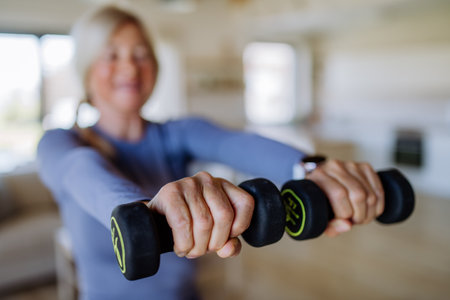 Fit senior woman exercising with dumbbells at home, active lifestyle concept.の写真素材