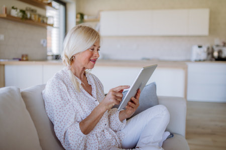 Senior woman sitting on sofa and rusing tablet at homeの写真素材