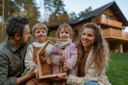 Happy family is standing near their modern house, smiling and looking at cameraの写真素材