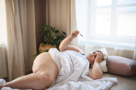 Sick overweight woman lying in bed at home.