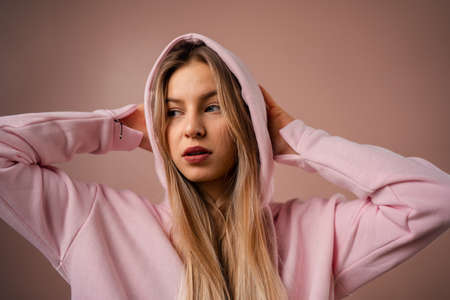 Fashion studio portrait of a happy young blonde woman in hoodie posing over pink background.の写真素材