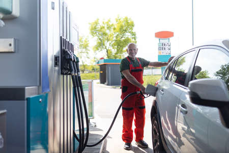 Senior worker standing on gas station and fueling car.