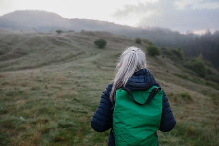 Rear view of senior woman hiking in nature on early morning with fog and mountains in background.の写真素材